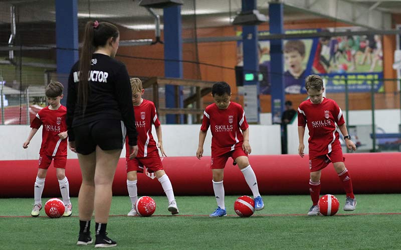 Several young boys perform a soccer skills drill while an instructor watches during a Skills Institute class at Arena Sports