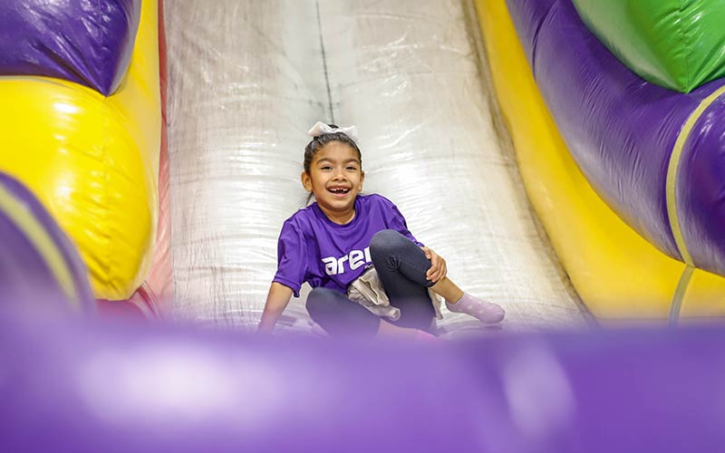 A girl smiles on the bouncy slide during Summer Camp at Arena Sports