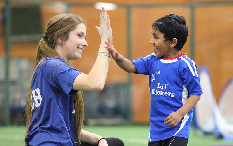 A coach and Lil Kickers student high five each other during soccer class