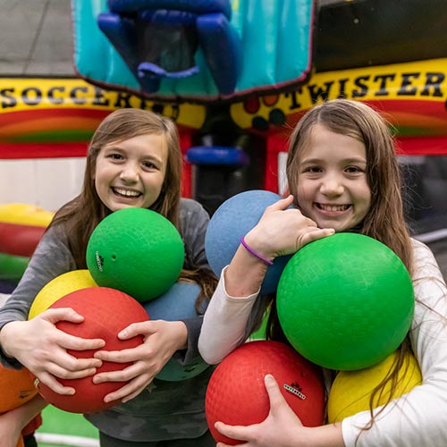 Two young girls hold rubber balls while in the Inflatable FunZone at Arena Sports SODO