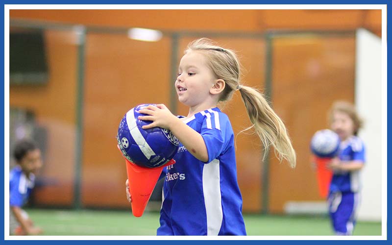 Children play with soccer balls and cones in a Lil' Kickers class