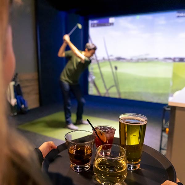 Waitstaff deliver drinks while a person preps their golf swing in the Golf Simulator at Arena Sports Issaquah