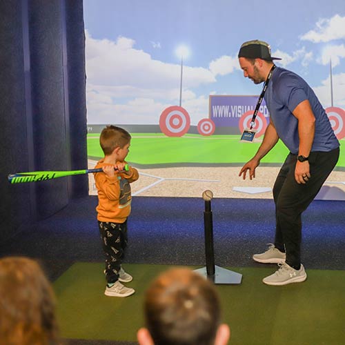 A dad and his young son practice Tee Ball in the Sports Simulator at Arena Sports Issaquah