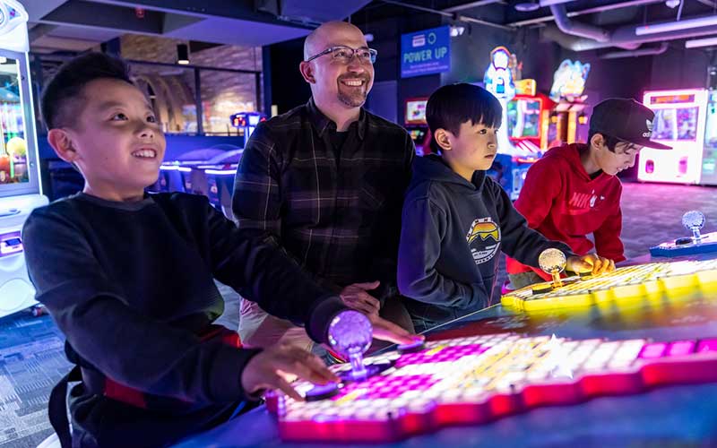 An adult and three boys play games in the arcade at Arena Sport